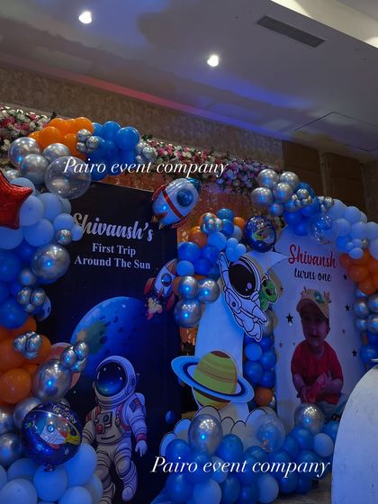 A close-up of the backdrop for Shivansh's "First Trip Around The Sun." The space theme is detailed with astronaut and planet cutouts, personalized banners, and a galaxy of blue, orange, and silver balloons.