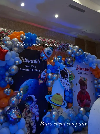 A close-up of the backdrop for Shivansh's "First Trip Around The Sun." The space theme is detailed with astronaut and planet cutouts, personalized banners, and a galaxy of blue, orange, and silver balloons.