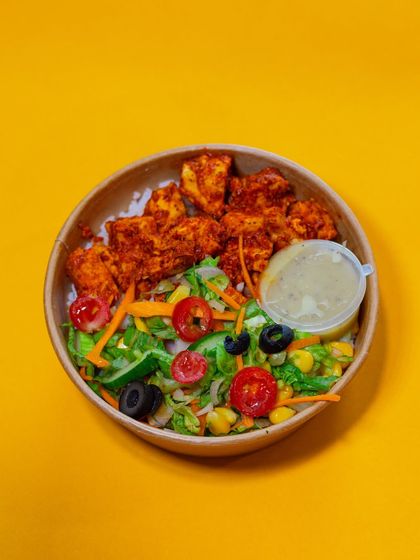 A top-down view of our fan-favorite Chicken Tikka Meal. You can see the juicy chicken tikka, a fresh side salad with tomatoes and olives, and our signature dressing, all ready to be mixed and enjoyed.