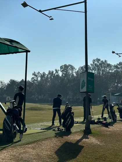 Golf bags line the edge of the practice area as players get their reps in on a sunny day.