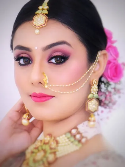 This look features a sleek, tight bun that provides a perfect canvas for the statement jewelry, including the nath and maang tikka. The pink floral accent adds a pop of color.
