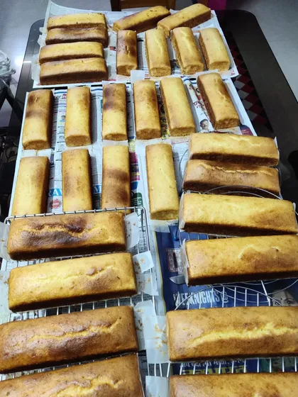 A behind-the-scenes look at my kitchen with a large batch of Mawa Rawa cakes cooling on racks. I bake everything fresh at home, ensuring each loaf is perfect.