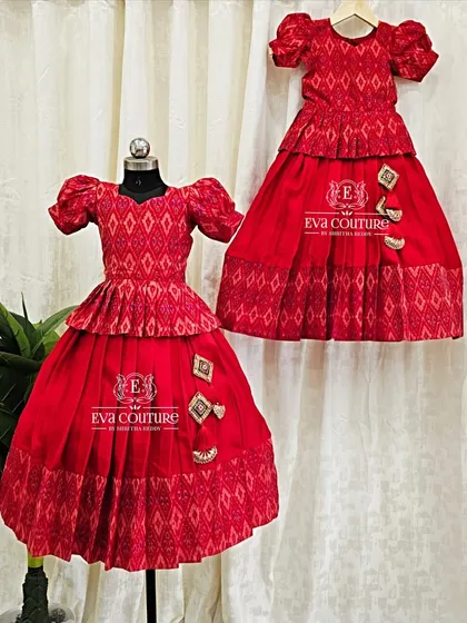 A matching set of two pattu pavadais in a striking red ikat fabric. Both outfits feature a peplum-style top and puffed sleeves, with slight variations in the embellishments to give each sister her own unique touch.