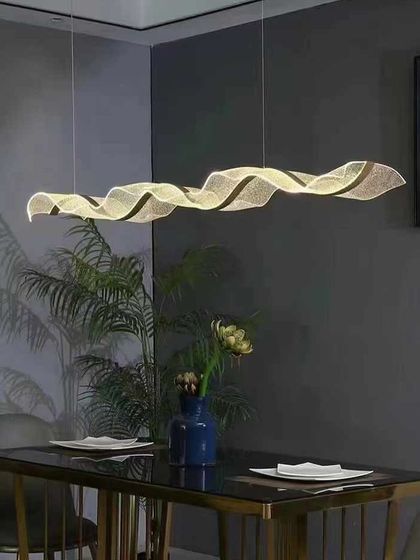 The ribbon pendant installed over a dining table, demonstrating how it can define a space with its clean lines and soft light.