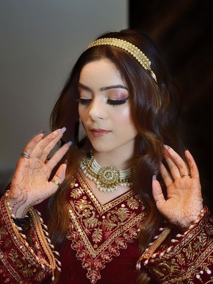 This portrait showcases the complete bridal or festive look, from the pearl choker to the henna on her hands. The soft, closed-eye pose highlights the beautiful eye makeup.