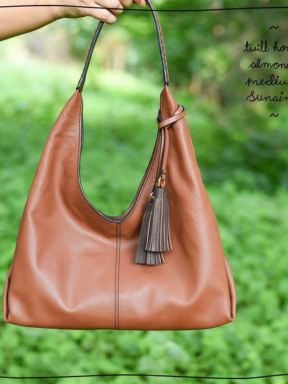 The Medium Sunaina hobo bag in our Twill Honey Almond edit. This version features a solid tan body with a contrasting twill-woven handle and tassels in Oak brown, adding a subtle, crafty detail to a classic design.
