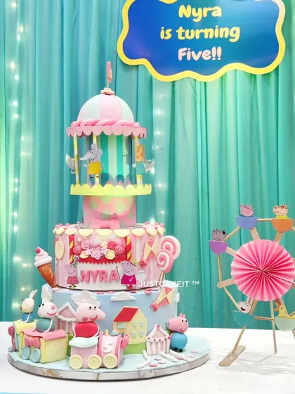 Another view of the magnificent Peppa Pig party cake, set up at the event. The multi-tiered design includes a train, a ferris wheel, and a carousel, creating an entire Peppa-themed amusement park.