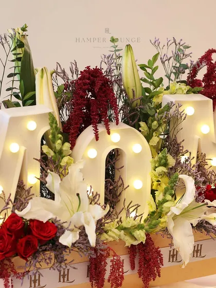 A closer look at the illuminated "MOM" hamper, focusing on the beautiful interplay of the warm lights and the fresh flowers.