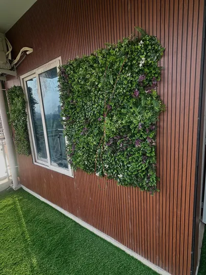 Artificial green wall panels are used as decorative accents around a window on a wood-paneled exterior wall.