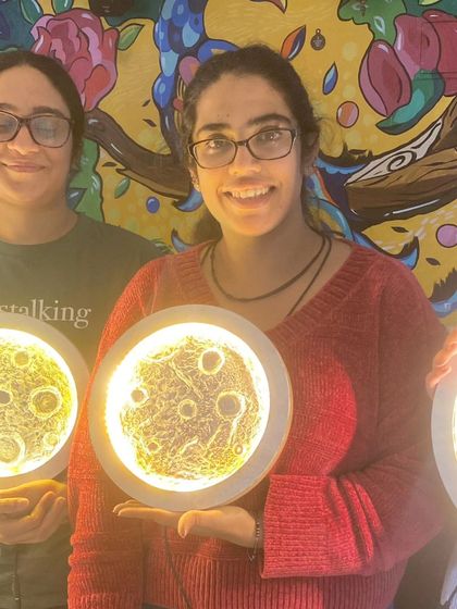 Two friends proudly showing their finished moon lamps. Our workshops are a perfect activity for a creative and memorable friends' day out.