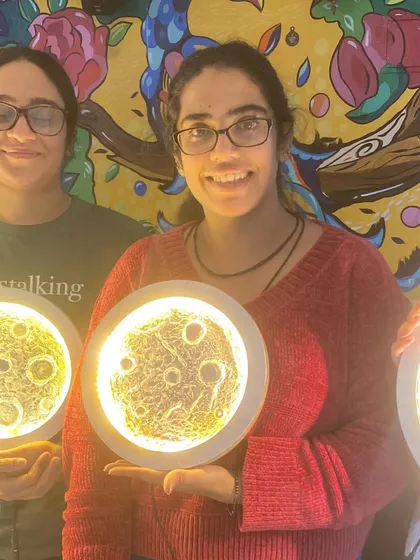 Two friends proudly showing their finished moon lamps. Our workshops are a perfect activity for a creative and memorable friends' day out.