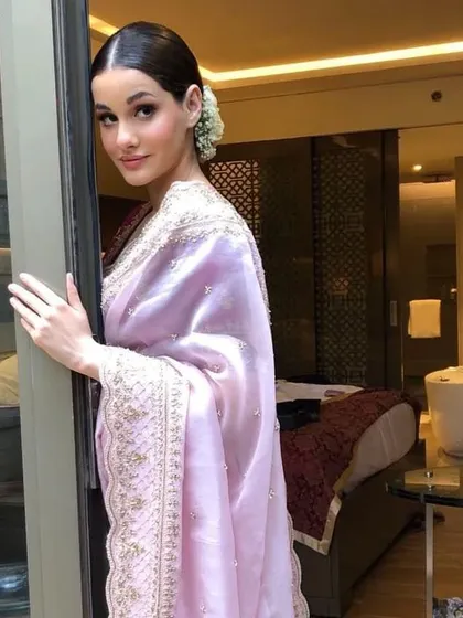 A bride looking out a window, her hair styled in a classic low bun with white roses. This is a timeless and romantic hairstyle for any wedding event.