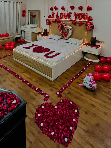 An elevated view of a romantic bedroom surprise, showing the heart-shaped arrangement of rose petals on the floor and the 'I ❤️ U' message on the bed. The layout is designed to be stunning from every angle.