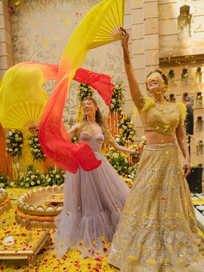 The bride and a friend dancing with colorful fans during a lively Haldi celebration. My goal is to create a festive atmosphere where everyone feels free to celebrate.