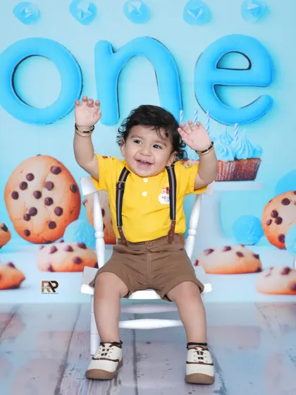 A joyful baby boy raises his hands in excitement during his cookie-themed photoshoot. His happy energy is contagious in this fun and colorful setting.
