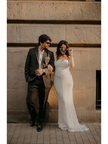 A cool, editorial-style photo of the couple leaning against a stone wall, showcasing their modern and stylish outfits.