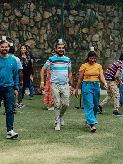 The Pyramid Builder challenge continues, with team members carefully walking to avoid dropping their cups.