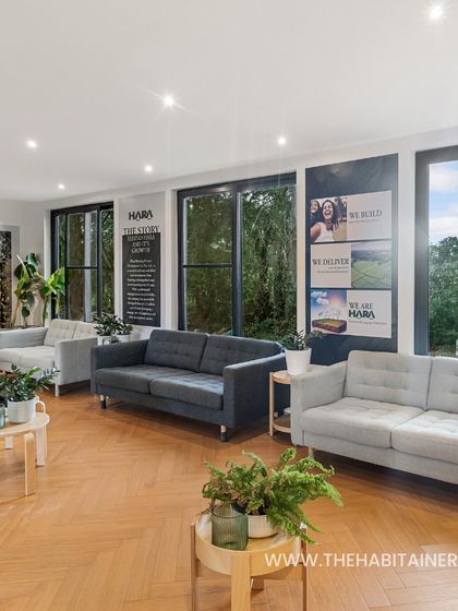 The interior of the HARA site office features a spacious lounge area with comfortable seating and herringbone wood flooring. Large windows and glass doors flood the space with natural light.