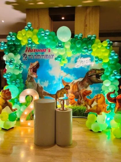Roar! A thrilling dinosaur-themed party for Haroon's 2nd birthday. The backdrop features realistic T-Rexes, surrounded by a green balloon arch and dinosaur balloon figures.