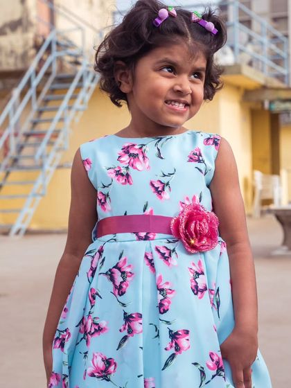 A lovely sky blue dress with a vibrant pink floral print. The matching pink sash with a flower detail ties the whole look together beautifully.