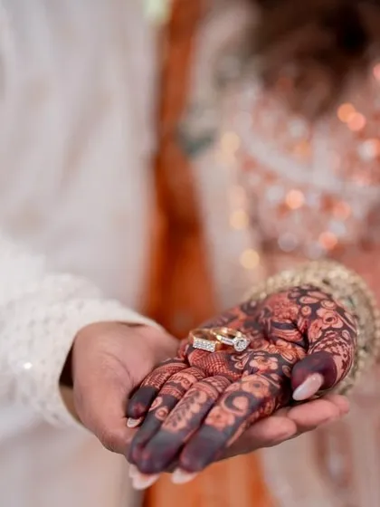 A beautiful moment captured, with the engagement rings resting on the richly stained henna, symbolizing the promise of a lifetime together.