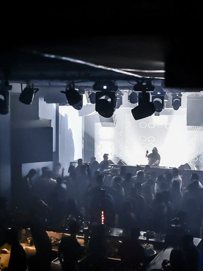 A black and white shot capturing the silhouette of the crowd against the bright stage lights. It shows the scale and atmosphere of a major club event.
