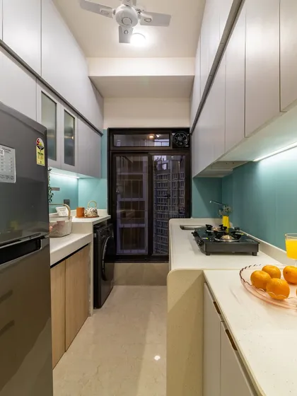 This galley kitchen feels spacious thanks to light-colored overhead cabinets, under-cabinet lighting, and a continuous countertop that wraps around the corner.
