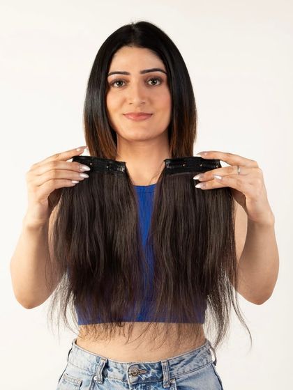 A model holding two pieces of clip-in hair extensions, clearly showing the product to the customer.