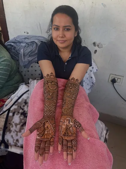 A lovely bride displaying her full bridal mehandi, featuring portraits of a bride and groom on her palms.