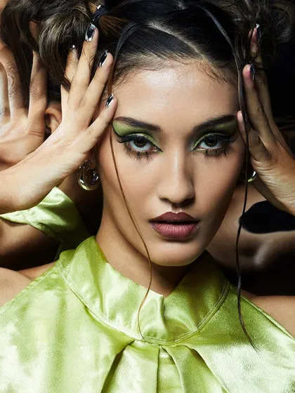 A dramatic green smokey eye with spiky lower lashes, paired with a matching green top for a cohesive, high-fashion look.