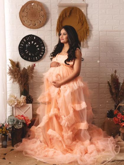 A full-length standing portrait showcasing a magnificent peach ruffled gown. This dress is perfect for clients who want a dramatic, high-fashion maternity look.