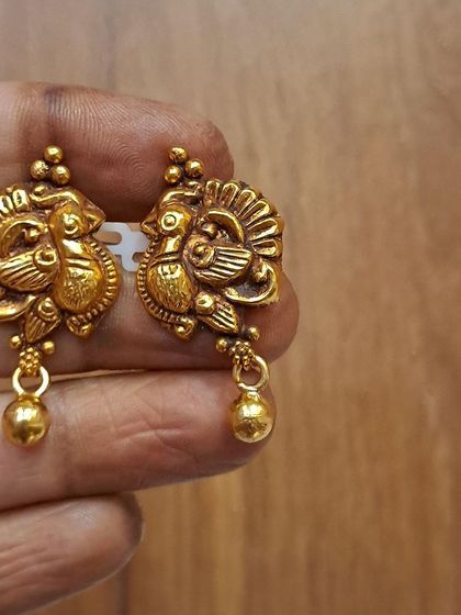 A beautiful pair of antique silver gold-plated earrings with a peacock motif. The small golden bead drop adds a touch of traditional charm.