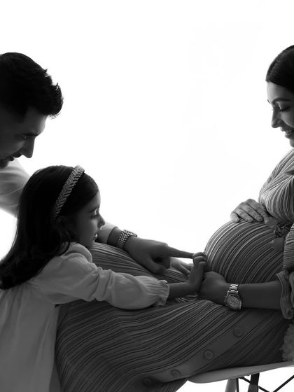 A beautiful black and white image of the family interacting with the baby bump. It's a story of connection told through gentle touch and loving gazes.