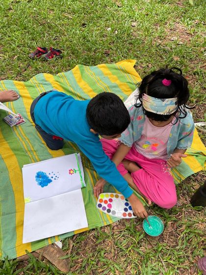 Two children collaborate on a watercolor painting project on the grass. Art and creativity are always encouraged in our story circle.