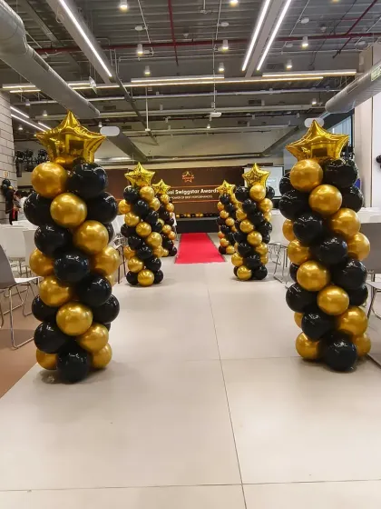 Here is another view of the balloon pillar arrangement for the Swiggy corporate event. The spiral design in the company's brand colors adds a touch of sophistication and visual interest to the large event hall.