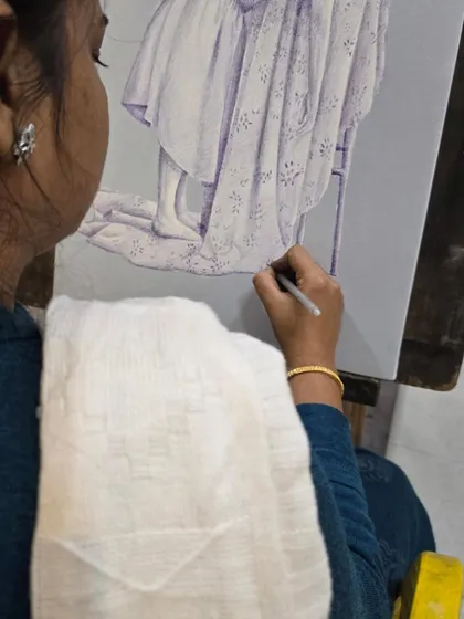 This shot highlights the artist's hand as she carefully renders the folds and patterns of a blanket in her ballpoint pen drawing.