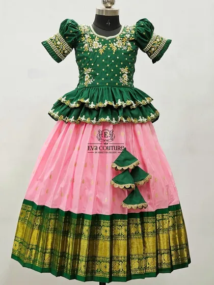 A classic green and pink Pattu Pavadai with a tiered peplum blouse and a rich gold Kanchi border.