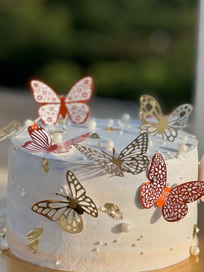 A beautiful white cake adorned with an array of delicate, laser-cut butterfly toppers in gold and red. This design is perfect for birthdays and adds a touch of enchantment.