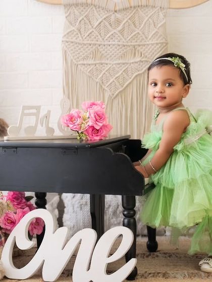A bright and happy first birthday portrait. This little girl in her lovely lime green dress stands proudly by her miniature piano, celebrating her special day.