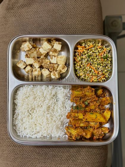 This plate features steamed rice with a side of seasoned tofu, sprouted moong salad, and a flavorful drumstick curry, offering a great mix of textures and nutrients.