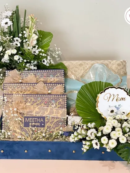 A complete trousseau hamper set for the family, featuring sweet boxes, beautifully wrapped gifts for "Mom," and stunning fresh floral arrangements in a classic white and blue theme.