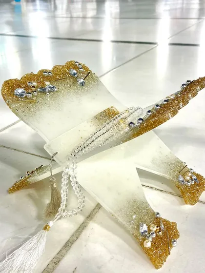 A close-up view of the white and gold Quran holder, highlighting the sparkling crystals and the delicate tassel of the tasbeeh. This piece combines elegance with devotion.