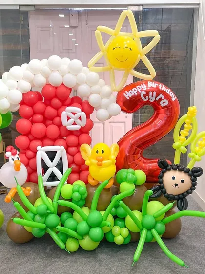 A detailed shot of the barnyard section of my farm animal display. The red barn, smiling sun, and little farm animals are all sculpted from balloons to create a charming and lively scene for a child's party.