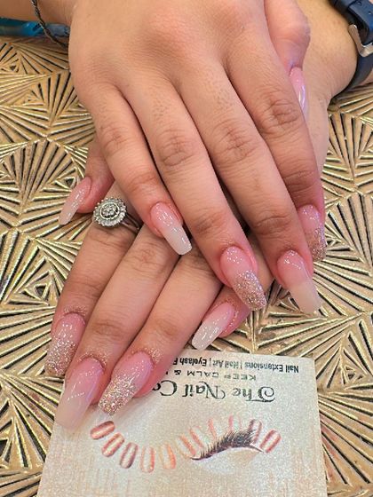 Extra-long coffin nails featuring a soft pink and nude ombre effect. The tips are dusted with gold glitter for a glamorous and elegant finish.