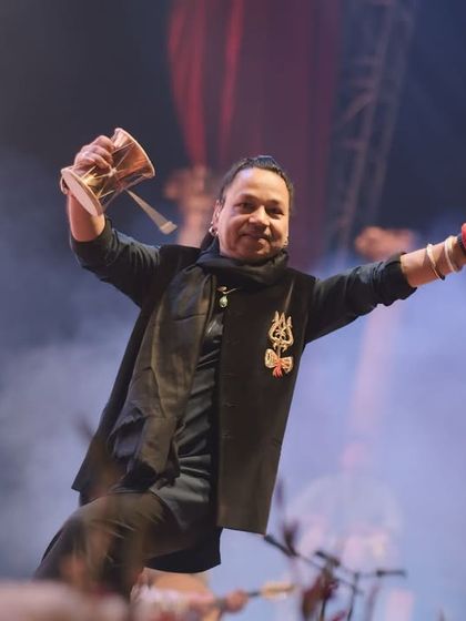 Kailash Kher celebrating on stage, damru in hand. This is a moment of pure joy and energy, a highlight from the Ganga Kinare Music Festival in Varanasi.