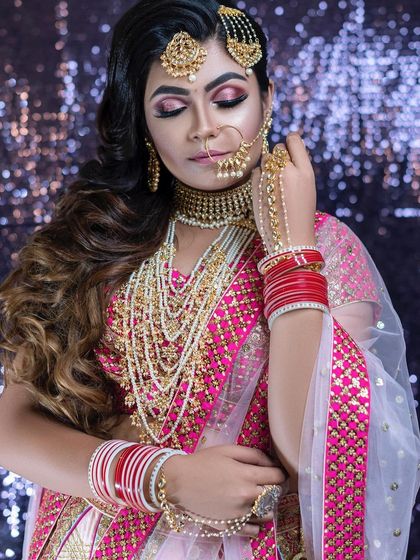This bride opted for soft waves cascading to one side instead of a traditional bun. The makeup features a beautiful pink and rose gold eyeshadow blend to match her lehenga perfectly.