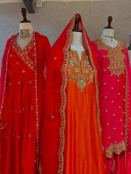 A vibrant display of red, orange, and pink suits perfect for the wedding season. The hooded red dupatta adds a touch of bridal drama.