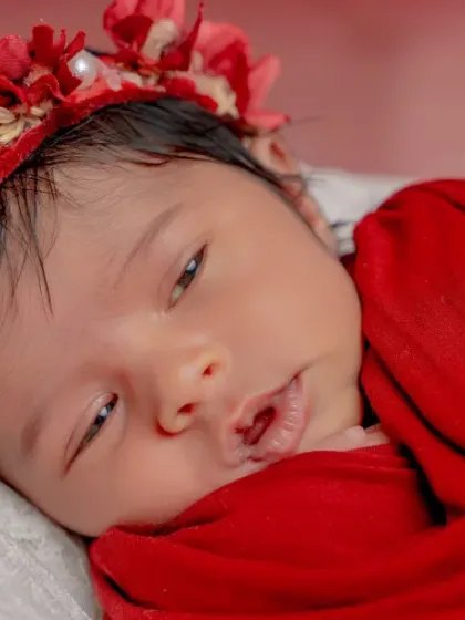 Wrapped in red and dipped in magic. This close-up shot shows the baby's beautiful face, framed by a red floral crown.