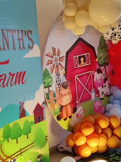 A charming farm-themed second birthday party. This setup includes a red barn backdrop, cow-print plinths, and a white picket fence, bringing a touch of the countryside to the celebration.