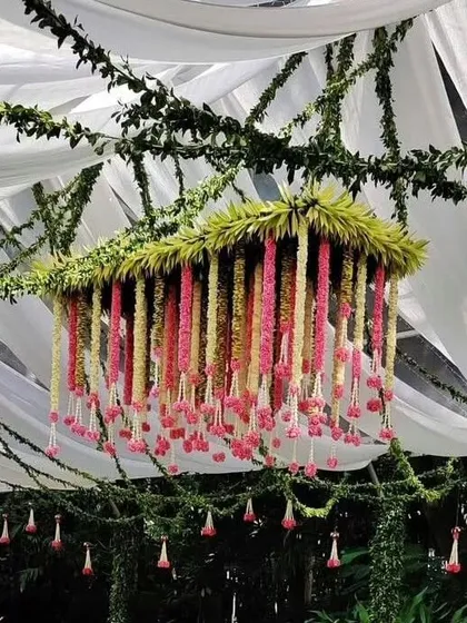 We use ceiling decor to create an immersive atmosphere. This floral chandelier, made with foliage and hanging strings of pink and yellow flowers, adds a touch of enchantment to this outdoor wedding setup.